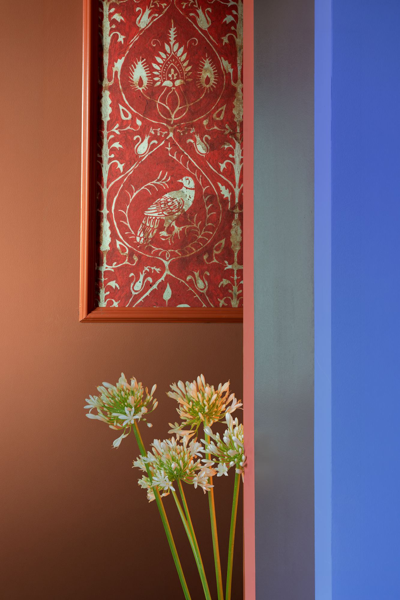 Red embroidered panel beside a blue wall with white agapanthus